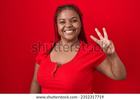 African american woman with braided hair standing over red background showing and pointing up with fingers number three while smiling confident and happy. 