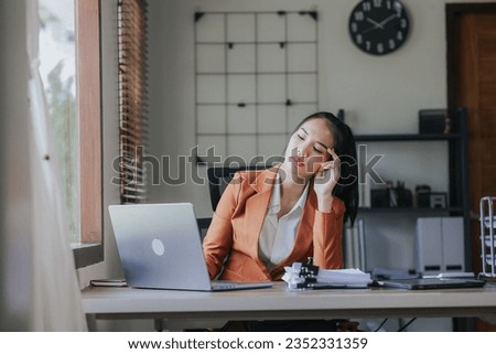 Asian businesswoman in brown suit sitting at desk in office