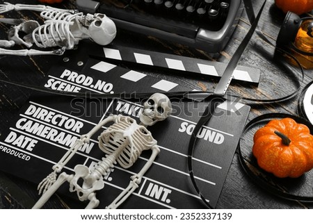 Typewriter with clapperboard, film reel and Halloween decor on black wooden background