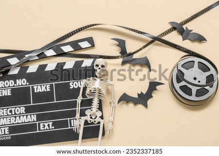 Clapperboard with film reel and Halloween decor on beige background