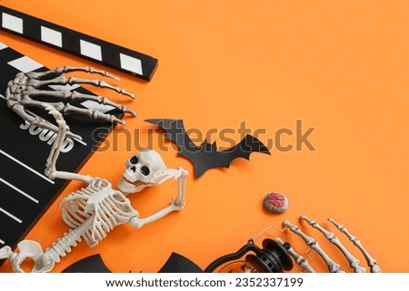 Clapperboard with different Halloween decor on orange background