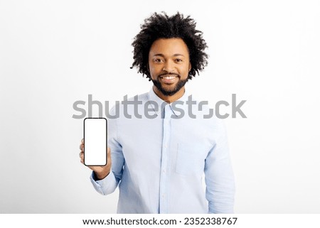 Friendly and smiling multiracial guy showing smartphone with empty blank screen, presenting new mobile app, male office employee in white formal shirt advertising