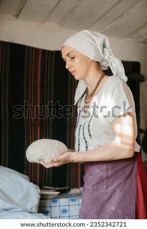 A woman in a Ukrainian embroidered dress holds a raw loaf of bread in her hands.