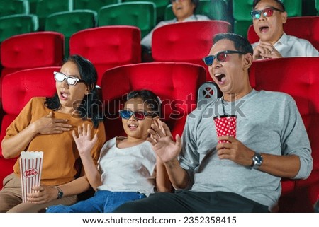 Happy Asian family of father, mother, daughter, and grandmother cherishes weekend moments at the cinema, sharing joy and togetherness while watching a movie.