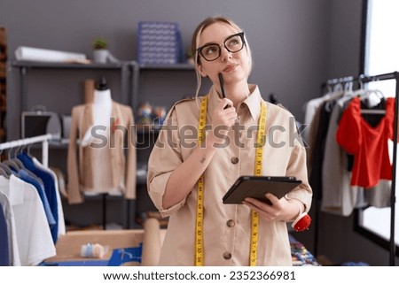 Young caucasian woman tailor using touchpad with doubt expression at atelier Royalty-Free Stock Photo #2352366981