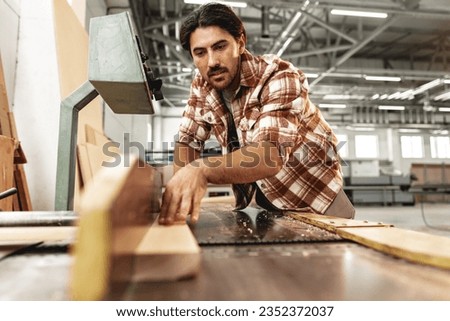 Young carpenter working on woodworking machines in the furniture factory