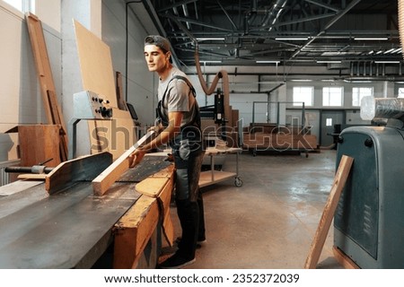 Young carpenter working on woodworking machines in the furniture factory Royalty-Free Stock Photo #2352372039