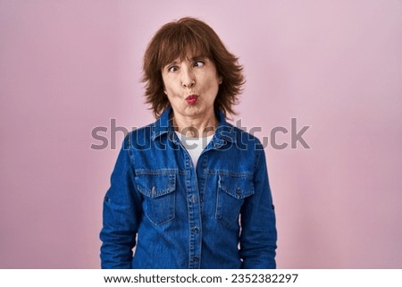 Middle age woman standing over pink background making fish face with lips, crazy and comical gesture. funny expression. 