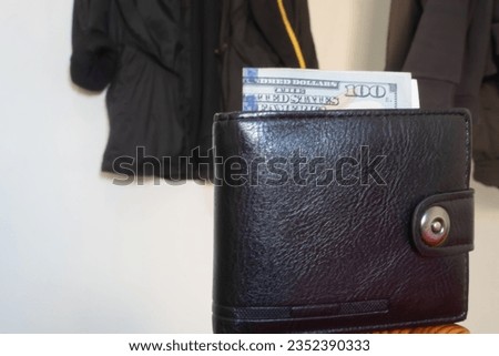 Last hundred dollar bill in the wallet against the backdrop of a half-empty wardrobe clearly shows how the poor live, who have all expenses planned in advance and they have no place to buy new clothes