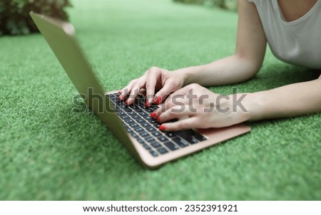 Woman lies on green lawn and works on laptop closeup