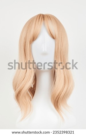 Natural looking blonde fair wig on white mannequin head. Middle length hair cut on the plastic wig holder isolated on white background, front view
