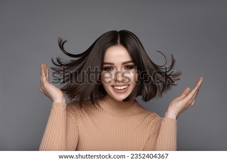 Portrait of pretty young woman with brown hair smiling on grey background