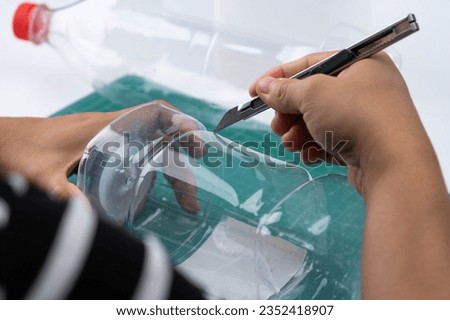 The process of making plant pots from plastic bottles. Hand cutting a plastic bottle with a cutter to grow plants or vegetables inside. Recycle and reusable green garden concept. Royalty-Free Stock Photo #2352418907