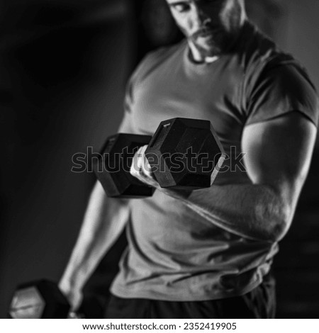 Black and white photo showcasing a handsome young man passionately engaged in a rigorous dumbbell workout, sculpting his physique