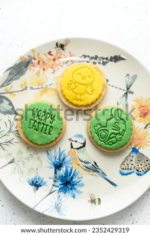 Two green and one yellow Easter cookies are placed on a plate with an intricate design, tabletop shot
