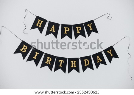 Black flags with golden letters with the inscription "Happy Birthday" on a white wall background. Horizontal format.