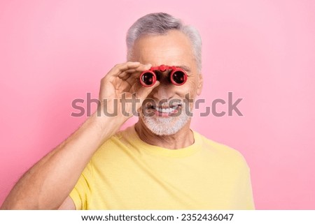Photo of curious senior man with gray beard dressed yellow t-shirt look in binoculars at theater isolated on pink color background