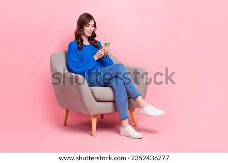 Full size photo of lovely young lady sit soft armchair hold device typing wear trendy blue garment isolated on pink color background