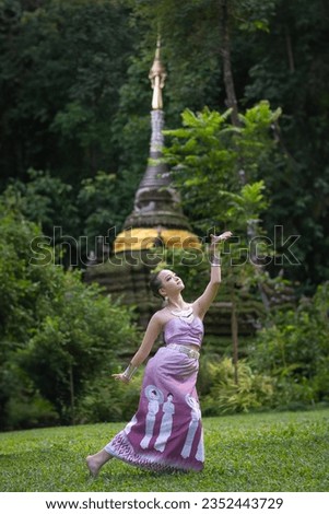 Pretty girl wearing beautiful traditional Thai dresses with the Thai Dance show in green natural at Wat Pha Lat Temple the famous place in Chiang Mai, Thailand. Concept of ancient Thai culture dance. Royalty-Free Stock Photo #2352443729
