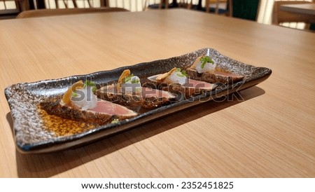 Tuna tataki with chopped garlic and celery leaves with soy sauce sauce served on a black square plate on a wooden table. Royalty-Free Stock Photo #2352451825