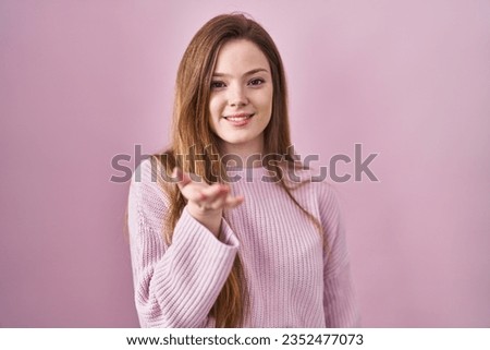 Young caucasian woman standing over pink background smiling cheerful offering palm hand giving assistance and acceptance. 