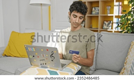 Young hispanic man shopping with laptop and credit card sitting on sofa at home