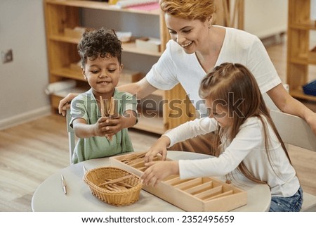positive multiethnic kids playing with wooden didactic materials near teacher in montessori school