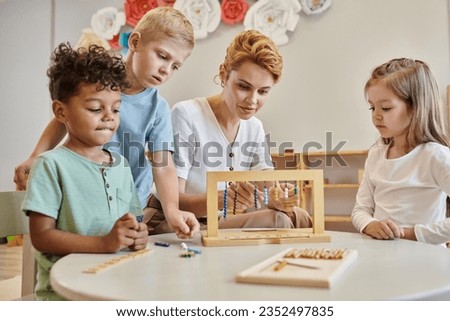 montessori school, female teacher observing interracial kids, playing educational game, diverse boys Royalty-Free Stock Photo #2352497835