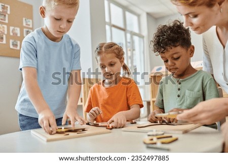 interracial kids playing with didactic montessori material near teacher in school, learn and play Royalty-Free Stock Photo #2352497885
