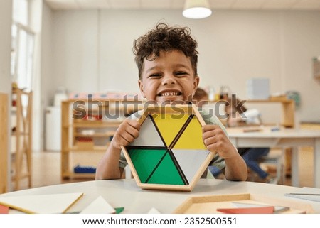 positive african american boy holding wooden didactic materials in blurred montessori school Royalty-Free Stock Photo #2352500551