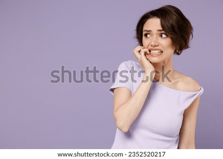 Young disappointed puzzled confused embarrassed woman 20s with bob haircut wear white t-shirt look aside biting nails isolated on pastel purple background studio portrait. People lifestyle concept. Royalty-Free Stock Photo #2352520217