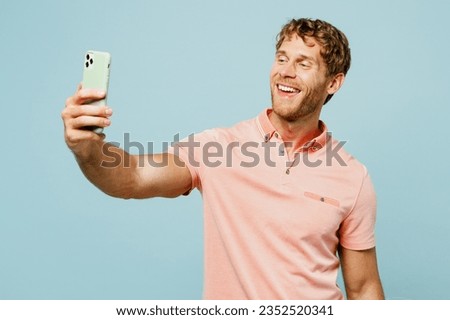 Young man he wear pink t-shirt casual clothes doing selfie shot on mobile cell phone post photo on social network isolated on pastel plain light blue cyan background studio portrait. Lifestyle concept