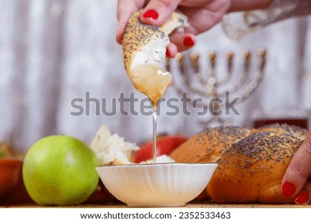 A woman's hand dips a piece of challah in honey on the Jewish holiday of Rosh Hashanah. Horizontal photo