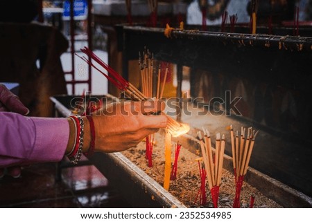 Picture holding incense sticks and bringing it near the fire on the candle. To light the incense stick and used for religious ceremonies.