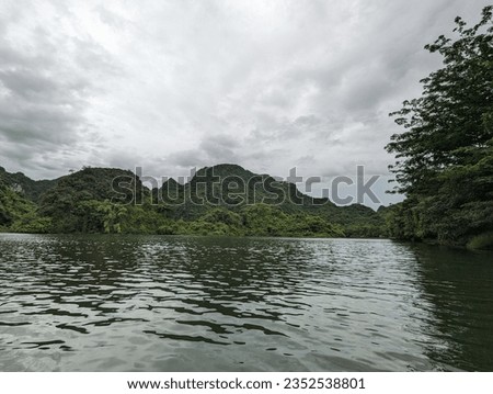 View of World heritage Tràng An Scenic Landscape Complex on a cloudy day with hills and river shore  in Northern Viet Nam