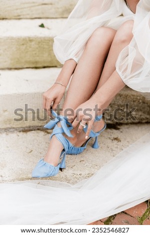 Stunning bride ties her beautiful powder blue heels on her wedding day on the steps of a historic building Royalty-Free Stock Photo #2352546827