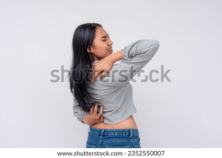A young asian woman struggles to reach her back. A futile attempt to scratch her back with her own hands, the acnestis. Royalty-Free Stock Photo #2352550007