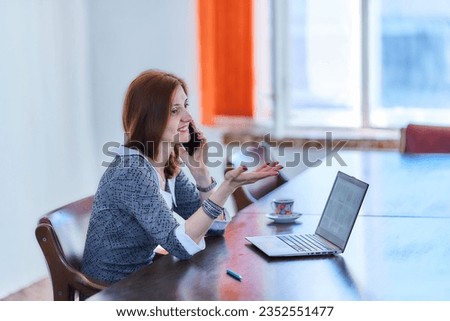 Young businesswoman working on laptop at office while talking on phone