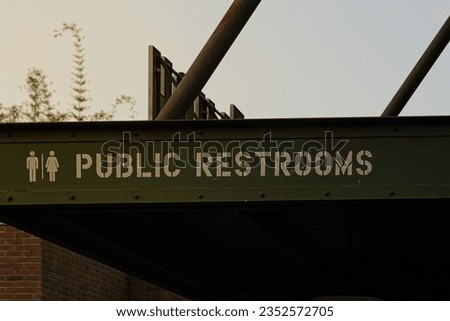 A public restrooms sign on a green metal structure in a clear sunset.