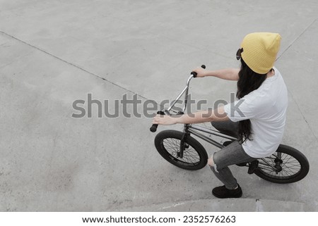 young woman sitting on a freestyle bike wearing yellow beanie, photo taken in