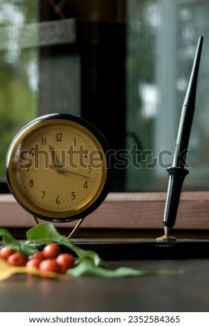 Vintage desk clock with ink fountain pen and apple tree leaves with small apples on wooden background with bokeh. Autumn season picture style.