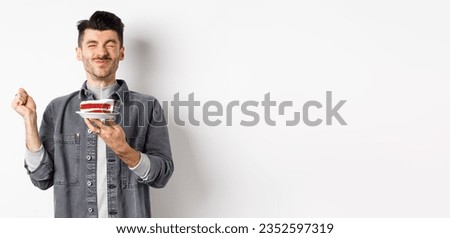 Happy birthday guy making wish on cake with candle, celebrating bday, standing on white background.
