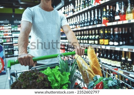 Cropped image of handsome young man pushing a shopping cart and choosing beverages in the supermarket