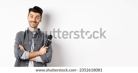 Handsome caucasian guy with moustache cross arms on chest, holding mic and smiling at camera, perform on stage with microphone, standing against white background.