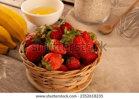 Bamboo basket filled with fresh ripe strawberries in a pink background above a wooden table horizontal