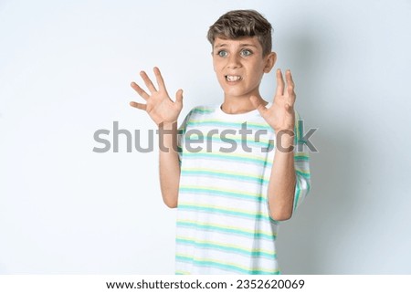 Beautiful kid boy wearing striped casual t-shirt afraid and terrified with fear expression stop gesture with hands, shouting in shock. Panic concept.