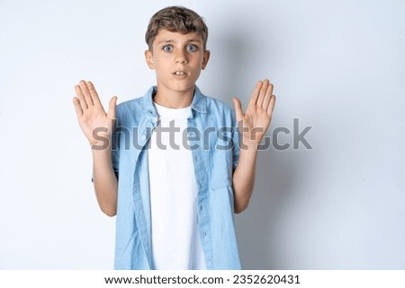 Serious Beautiful kid boy wearing casual clothes pulls palms towards camera, makes stop gesture, asks to control your emotions and not be nervous