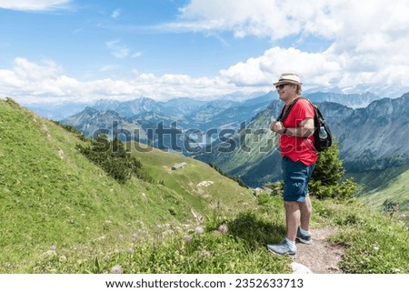 Senior man with sunglasses, cap and backpack on a mountain with the Swiss Alps in the background
