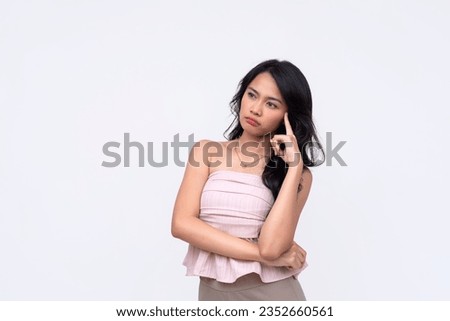 An undecided young asian woman feels confused while considering her options. A puzzled lady in thought looking to the left. Isolated on a white background. Royalty-Free Stock Photo #2352660561
