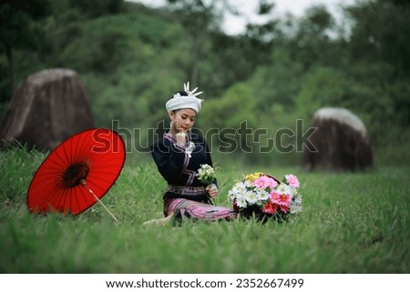 natural light portrait of asian young woman sitting on green grass wearing traditional thai culture lanna dress style and basket of flowers and her red umbrella in the natural garden, forest 
 Royalty-Free Stock Photo #2352667499